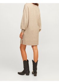 Beige neulemekko, jossa on pitkät puff-hihat, sivuhalkiot ja ribbireunus, yhdistetty mustiin cowboy-kengiin, joissa on kohokuviointia.