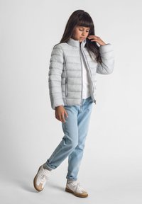 Grå puffjacka med horisontell sömnad, dragkedjestängning och sidofickor. Bärs med blå jeans och vita sneakers med bruna sulor.