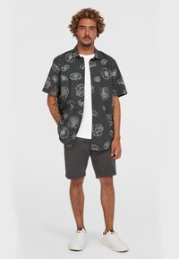 Kortærmet sort skjorte med hvide grafiske tryk, parret med grå shorts og hvide sneakers. Skjorten har en afslappet pasform og en krave.