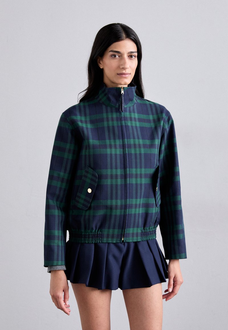 Giacca a quadri blu e verde con colletto alto, zip dorata e fascia elastica in vita. Presenta tasche frontali e un design elegante.