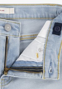 Φωτεινό μπλε τζιν παντελόνι με φερμουάρ, κίτρινα ραφές, κουμπώματα τύπου σναπ και εσωτερική επένδυση από ύφασμα σε λευκό με μπλε λεπτομέρειες.