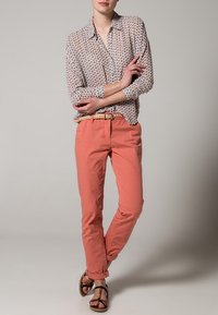 Camicia a maniche lunghe, con bottoni, di base bianca e piccoli accenti a motivo. Abbinata a pantaloni corallo e sandali marroni. Tessuto texturizzato.