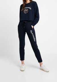 Conjunto de sudadera y joggers en color navy, hecho de una mezcla de algodón. La sudadera cuenta con bordado del logo; los joggers tienen bolsillos laterales y una cintura con cordón.