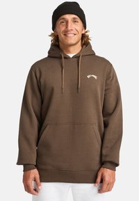 Brauner Hoodie mit verstellbaren Kordeln, Fronttasche und gerippten Bündchen. Mit Logo in weißem Text auf der oberen linken Brust.