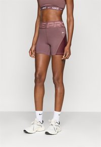 Αθλητικό σουτιέν Nike Pro και αντίστοιχα σορτς σε απαλή απόχρωση μουβ, με υφασμάτινη επένδυση και λογότυπα της μάρκας σε αντίθετα χρώματα.