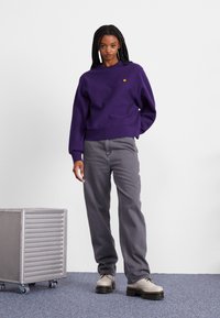 Purple sweatshirt with a crew neckline, relaxed fit, and ribbed cuffs, paired with high-waisted gray jeans and cream platform shoes.