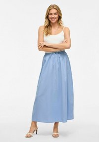 Lichtblauwe maxi-jurk met een elastische tailleband en een trekkoord, met een zachte textuur en A-lijn ontwerp. Gecombineerd met een wit tanktop.