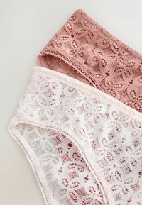 Deux ensembles de lingerie en dentelle florale, rose clair et rose poudré, superposés en diagonale sur un fond neutre.