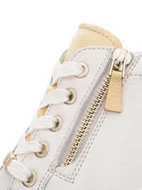 Zbliżenie na przód białego, skórzanego sneakersa z białymi sznurowadłami, metalowymi przelotkami oraz złotym bocznym suwakiem z skórzanym uchwytem.