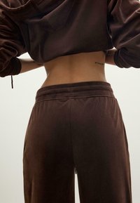 Brązowy welurowy hoodie o skróconym fasonie z dopasowanymi luźnymi spodniami. Zauważalne detale przeszycia przy pasie. Gładka faktura.