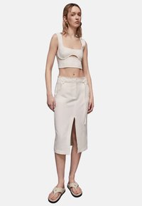 Cropped top bianco con un'apertura, abbinato a una gonna midi bianca con uno spacco frontale e tasche, completato da sandali leggeri.