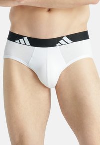 Weiße Unterhosen aus weichem Stoff mit einem schwarzen elastischen Bund, der drei weiße Streifen aufweist. Entwickelt für Komfort und Unterstützung.