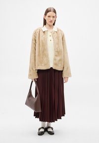 Casaco de pele sintética bege com aplicações florais, top de malha creme, saia plissada cor de vinho, mala castanha e sapatos pretos com detalhes dourados.