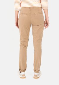 Beige chinos med en slank design, der har to baglommer, opbøjede ben og er parret med hvide sneakers. Glat stof, afslappet pasform.