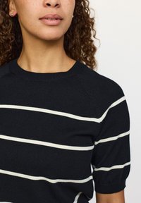 Črn pleten pulover z belimi vodoravnimi črtami, okrogel izrez, kratkimi rokavi in subtilnimi rebrastimi detajli na ovratniku ter rokavih.