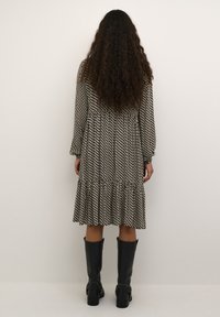 Robe à motifs noir et blanc avec des manches longues, un ourlet volanté et un tissu texturé. Portée avec des bottes noires jusqu'aux genoux.