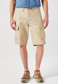 Pantaloni cargo beige con più tasche, realizzati in tessuto leggero. I pantaloni hanno una vestibilità rilassata e arrivano sopra il ginocchio.