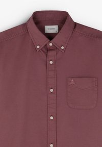 Bordeauxfarbendes Hemd mit Knopfleiste und kragen, ausgestattet mit weißen Knöpfen, einer Brusttasche mit einem Totenkopf-Logo und einer glatten Stofftextur.