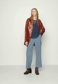 Casaco de couro castanho, blusa texturada azul-marinho, calças amplas azul-claro e botins castanhos de salto. Design simples com elementos sobrepostos.