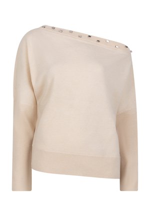 Beige gebreide trui met een asymmetrisch ontwerp, voorzien van een wijd decolleté en decoratieve metalen accenten langs de schouder. Lange mouwen.