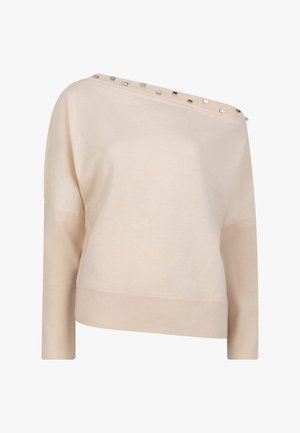 Beige gebreide trui met een asymmetrisch ontwerp, voorzien van een wijd decolleté en decoratieve metalen accenten langs de schouder. Lange mouwen.