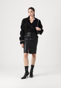 Μαύρο φανελένιο παλτό με βαθύ V-λαιμό, κλείσιμο με κουμπιά, συνδυασμένο με μαύρη ψεύτικη δερμάτινη φούστα με μπροστινή σχισμή και ζωνάκι στην μέση. Μαύρες μποτάκια μέχρι τον αστράγαλο.