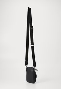 Black leather crossbody bag with a textured surface, zip closure, and adjustable strap featuring the brand name in black lettering.