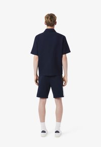Polo a maniche corte blu navy abbinato a pantaloni corti coordinati. L'outfit presenta un tessuto strutturato e una vestibilità comoda, completato da dettagli bianchi.