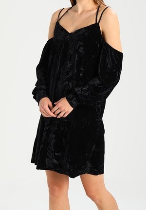 Black velvet dress with cold-shoulder design, long sleeves, and thin spaghetti straps. Features a relaxed fit and soft texture.