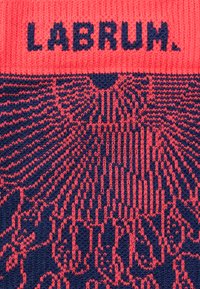 Gebreide muts met een heldere koraalkleurige band en een marineblauwe body met ingewikkelde patronen en de tekst "LABRUM" duidelijk zichtbaar.