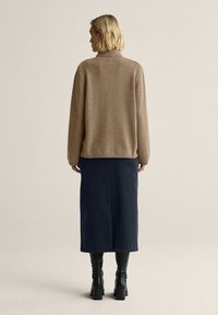 Beige neulepaita korkealla kauluksella, yhdistettynä tummansiniseen nilkkapituiseen hameeseen ja mustiin polven korkeisiin saappaisiin. Silkkinen pinta.