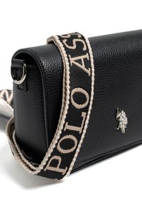 Borsa nera in tessuto con forma rettangolare. Presenta un logo argentato e una tracolla beige con la scritta "POLO". Accessori in metallo lisci.