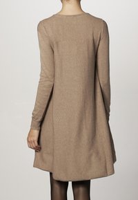 Abito lungo a maniche, in tessuto a maglia beige, con scollatura rotonda e trama sottile. Lunghezza a metà coscia, senza stampe o decorazioni visibili.