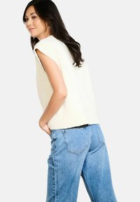 Kraftīga krēmu krāsas bezpagasta džemperis, kas savienots ar gaismas zilu augsto jostasvietu džinsu, kuriem ir brīvs piegriezums un smalki nolietojuma detaļas.