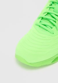 Neon-grüner Sportschuh mit strukturiertem Obermaterial, glattem Außensohle und Schnürverschluss. Verfügt über Rillen und Linien für ein dynamisches Design.