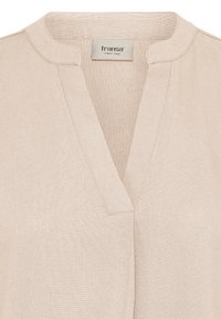 Vêtement en lin beige avec un col rond et une encolure en forme d'encoche en V, avec une étiquette en tissu portant le nom de la marque "fransa" cousue à l'intérieur.