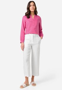 Rosa Leinenbluse mit langen Ärmeln und halber Knopfleiste, kombiniert mit weißen weit geschnittenen Hosen und beigen Sandalen. Glatte Texturen und taillierte Passform.