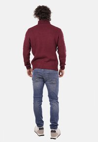 Maglione a collo alto a maglia bordeaux con un motivo testurizzato, abbinato a jeans azzurri chiari e sneakers bianche. Mostrato di spalle.