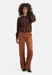 Zwarte sweater met een oranje luipaardprint en geribbelde manchetten, gedragen met roestkleurige wijde broeken. Modellen dragen zwarte hoge hakken.