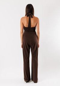 Jumpsuit marrone con scollo halter, caratterizzato da un corpetto smock e un design a gamba larga. Tessuto liscio con una vestibilità comoda, accentuato da un dettaglio al collo annodato.