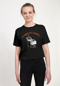 Sort t-shirt med et grafik af en mand, der skubber en indkøbsvogn. Teksten ovenfor lyder "BUBBLE'S DEPO" i orange. Klassisk crew neck design.
