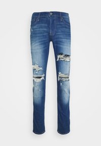Denimjeans in einem mittelblauen Waschung mit distressed Rissen und fransigen Kanten. Gerade Bein Design, Fünf-Taschen-Stil, mit Metallknopfverschluss.