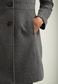 Grå ullkappa med skräddarsydd design, knappstängning och sidofickor med en mjuk, strukturerad yta.