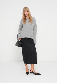 Grijze gebreide trui met een losse pasvorm, gecombineerd met een zwarte denim maxi rok. Accessoires zijn een kleine zwarte handtas en zwarte hakken.