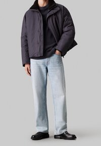 Puffjakke i mørkegrå med en blød sort pelskrave, parret med lyseblå lige ben jeans og sorte sko.