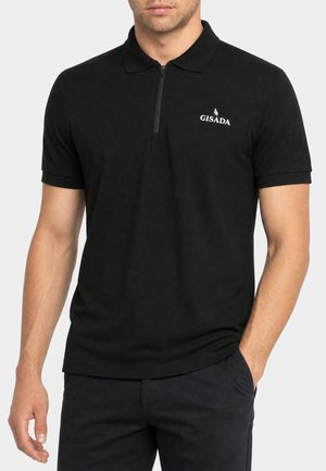 Uomo che indossa una polo nera a maniche corte con cerniera frontale e logo "GISADA" sul lato sinistro del petto, con una mano in tasca.