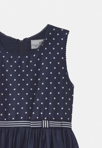 Laivansinis olkaimeton mekko valkoisilla pilkuilla, texturoitu kangas, kauniisti aaltoileva kaula-aukko ja raidallinen vyötärö, jossa on takana vetoketjukiinnitys.