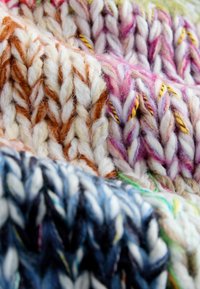 Krupni plan debelog, višebojnog pletiva u narančastim, ružičastim i plavim tonovima s vidljivom teksturom i ispletenim uzorcima.