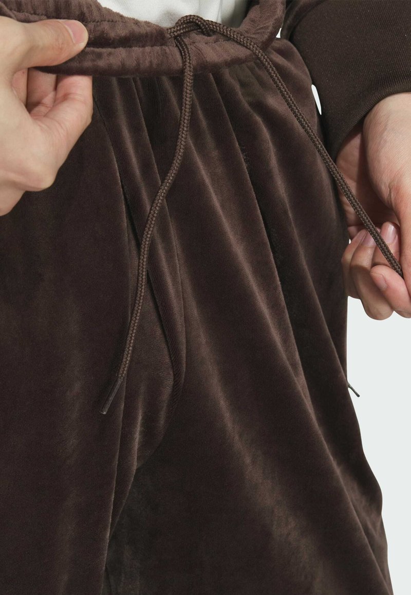 Handen passen het bruine koord aan van zachte, fluwelen donkerbruine broeken met een elastische tailleband.