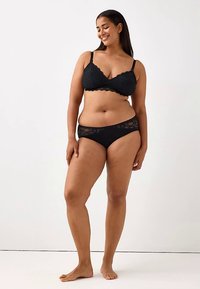 Svart spetsbralette och matchande trosor med vågiga kanter och blommönster. Tyget verkar mjukt med minimala metallaccenter.